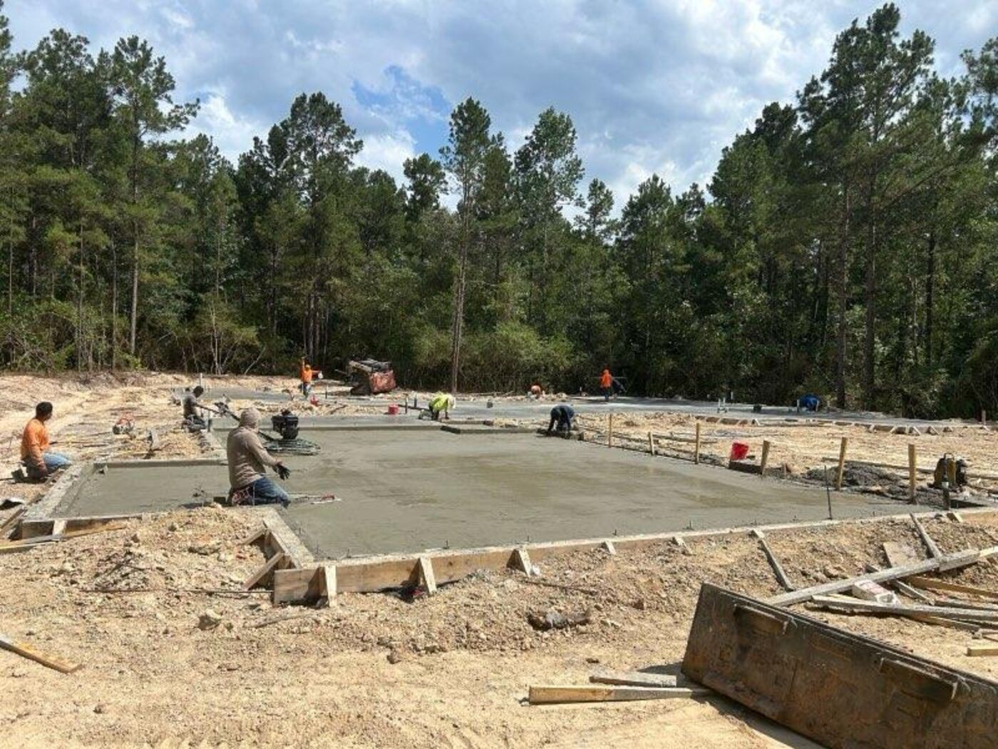 The freshly poured slab foundation with the crew finishing it, surrounded by Magnolia pine forest.
